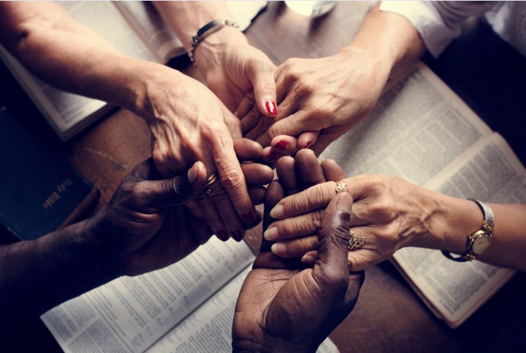 Hands clasped together in prayer over an open Bible